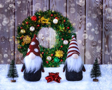 Foto de Dos gnomos de Navidad (elfos) en el fondo de una corona de Navidad, cinta roja y árboles de Navidad artificiales. Feliz concepto de Navidad con bokeh - Imagen libre de derechos