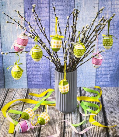 Foto de Colorful Easter eggs on willow branches. Easter tree in a vase with festive ribbons on a blue background. - Imagen libre de derechos