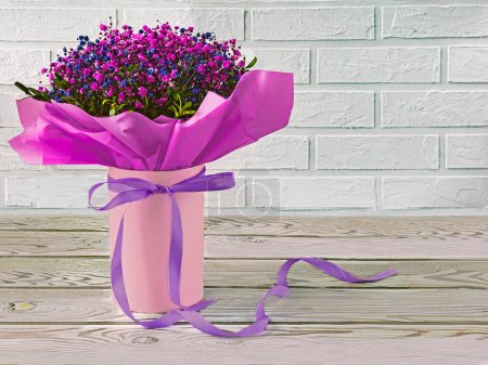 Foto de Un ramo festivo de flores de gypsophila púrpura y azul sobre un fondo de madera y ladrillo. Cinta de lavanda como decoración - Imagen libre de derechos