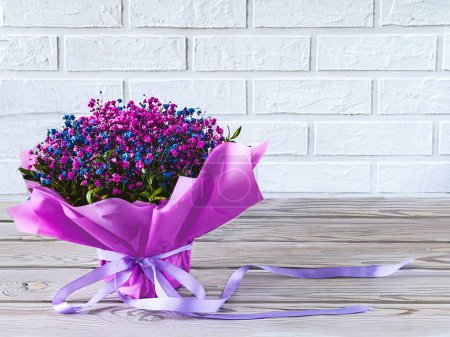 A bouquet of gypsophila flowers, a viva-magenta cup. Festive still life in purple colors on a wooden and brick background.