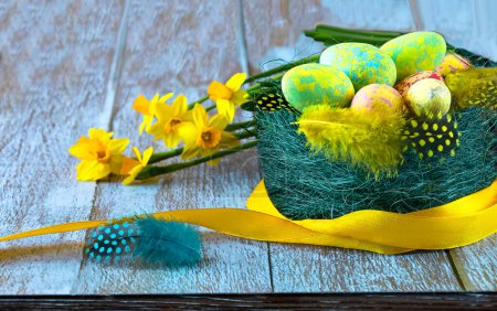 Foto de Nido con huevos y plumas de Pascua, flores de narciso amarillo y cinta amarilla, vista de cerca. Feliz concepto de Pascua. - Imagen libre de derechos