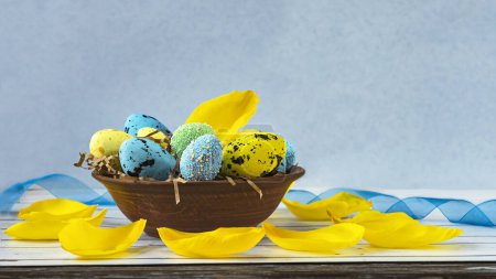 Téléchargez les photos : Assiette vintage aux œufs de Pâques bleus et jaunes et aux pétales de tulipes sur fond bois clair. Composition printanière en bleu et jaune. Vue latérale. - en image libre de droit