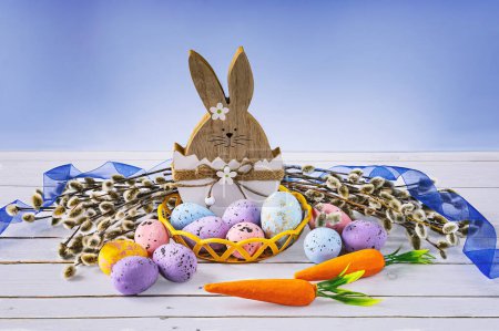 Téléchargez les photos : Lapin de Pâques aux œufs de Pâques, carotte et saule et ruban bleu. Composition festive de Pâques sur fond bleu. - en image libre de droit