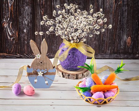 Téléchargez les photos : Lapin de Pâques avec œufs de Pâques et carottes. Un bouquet de brindilles de saule dans un vase comme décoration. Composition festive sur fond de bois. - en image libre de droit