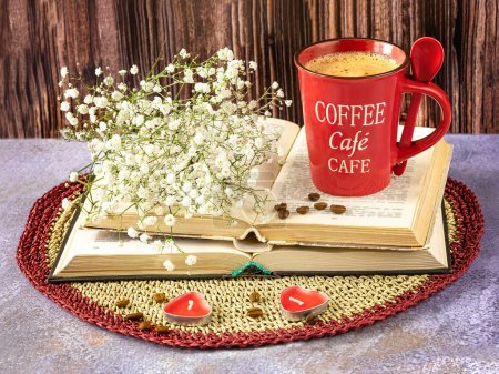Foto de Naturaleza muerta con una taza roja de café, libros, flores de gypsophila y granos de café. Velas como decoración. - Imagen libre de derechos