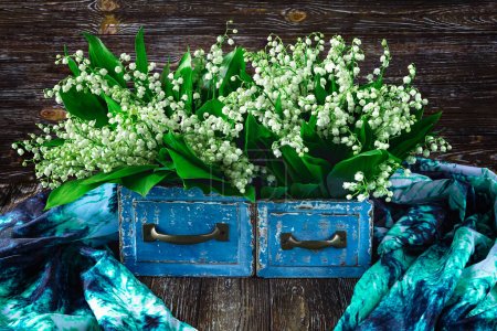 Foto de Un ramo de fragantes lirios del valle florece en una caja vintage azul y una bufanda azul sobre un fondo de madera. Primavera naturaleza muerta - Imagen libre de derechos