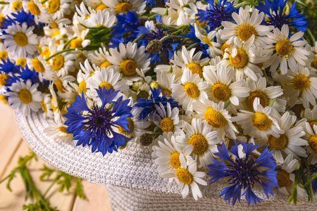 Photo for A bouquet of daisies and cornflowers in a sun hat. Summer background with wild flowers, top view - Royalty Free Image