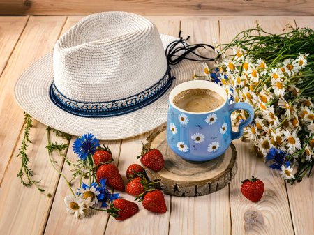 Photo for A blue cup of coffee with daisies, a bouquet of daisies and cornflowers, strawberries, sun hat. Summer still life with wildflowers, top view - Royalty Free Image