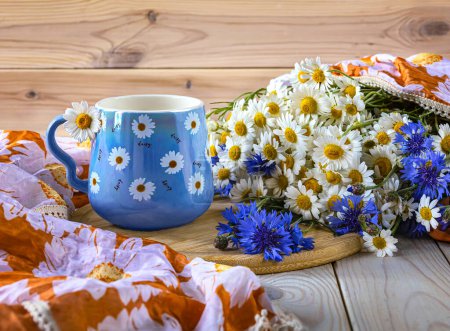 Foto de Una taza azul con margaritas y un hermoso ramo de margaritas y acianos. Naturaleza muerta de verano con flores silvestres - Imagen libre de derechos