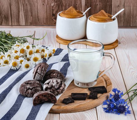 Foto de Galletas de chocolate en una bandeja, un vaso de leche fresca y chocolate. Desayuno en la mesa, flores de verano como decoración. - Imagen libre de derechos