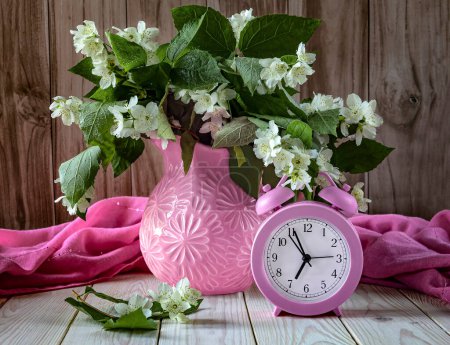 Foto de Bodegón de verano con un reloj despertador rosa, un ramo de flores de jazmín sobre la mesa. Hola concepto de verano - Imagen libre de derechos