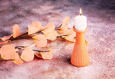 Foto de Una rama de flores artificiales en el color del año 2024 Melocotón Fuzz sobre un fondo de hormigón y un candelabro con una vela ardiente. Composición monocromática - Imagen libre de derechos