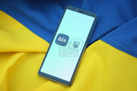 Photo for Kharkiv, Ukraine - October 18, 2022: Diia application on the smartphone screen against the background of the flag of Ukraine. Action is a mobile application with a web portal and a brand of e-government in Ukraine for citizens. - Royalty Free Image