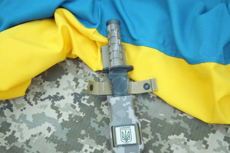 Cuchillo militar y etiqueta con un tridente sobre un fondo de camuflaje pixel. Guerra en Ucrania.