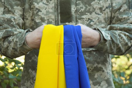 A Ukrainian military man holds the national flag in his hands as a symbol of strong. War in Ukraine. Day of the Cossacks and Defender of Ukraine.