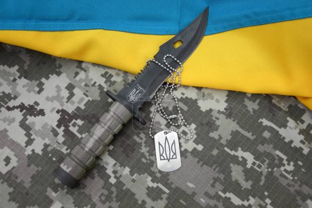 Cuchillo militar y etiqueta con un tridente sobre un fondo de camuflaje pixel. Guerra en Ucrania.