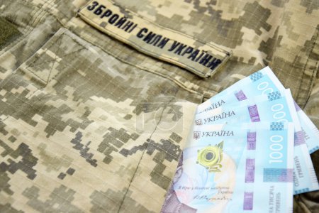 Ukrainian UAH banknotes against the background of a military pixel, the uniform of the military forces of Ukraine. The concept of salaries, payments and donations to the military.