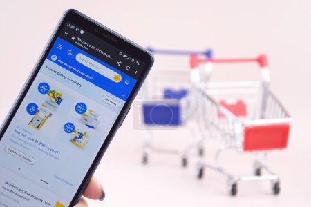 Photo for Kharkiv, Ukraine, MARCH 31, 2023: Shopping cart with a smartphone opened Walmart logo on the screen on a blue background. - Royalty Free Image