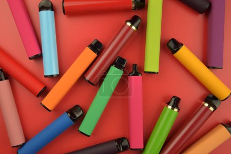 Set de cigarrillos electrónicos desechables multicolores sobre fondo rojo. El concepto de tabaquismo moderno, vapeo y nicotina.
