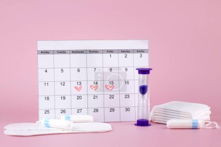 Women's menstrual pads, tampons, female menstruation calendar and alarm clock on a pink background. Period of critical days. Place for text.