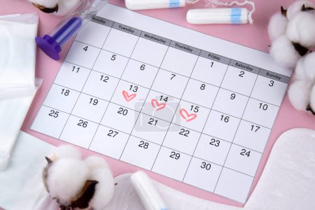 Women's menstrual pads, tampons, female menstruation calendar and alarm clock on a pink background. Period of critical days. Place for text.