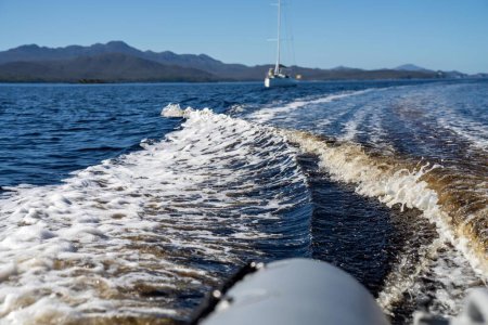 Photo for Tinny dinghy boat on the water making a wake behind a boat making waves on a river in a national park in australia. beach in summer - Royalty Free Image