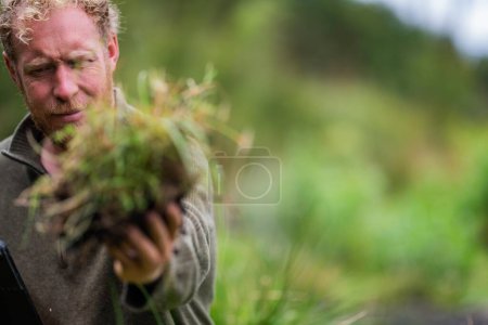 Téléchargez les photos : Agriculteur Tenant le sol dans une main, se sentant compost dans un champ en Tasmanie Australie. spécialiste des sols en Australie - en image libre de droit