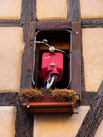 Foto de Riquewihr, Francia - 12 de octubre de 2022: Vespa Roja en la ventana de la casa tradicional en Alsacia - Imagen libre de derechos