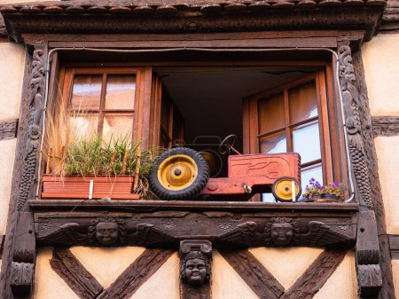 Foto de Riquewihr, Francia - 12 de octubre de 2022: Modelo de tractor rojo en la ventana de la casa tradicional en Alsacia - Imagen libre de derechos