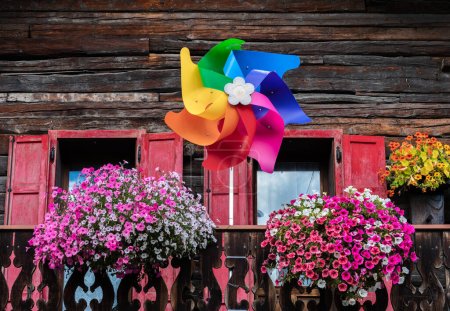 Der Balkon eines Holzhauses in Livigno, Italien, mit einem Regenbogen-Windrad und Blumenschmuck