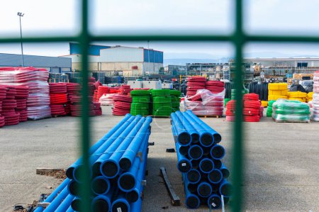 Téléchargez les photos : Une vue à travers une clôture à un entrepôt de tuyaux et de matériaux en plastique industriels colorés - en image libre de droit