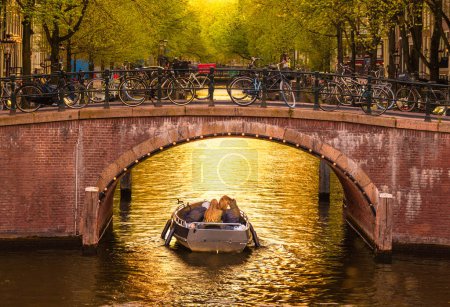 Ámsterdam, Países Bajos - 24 de abril de 2022: Un grupo de jóvenes disfrutando de las reflexiones de la hora dorada en un canal en Ámsterdam, Países Bajos, rodeado de impresionantes puentes de arco y arquitectura.