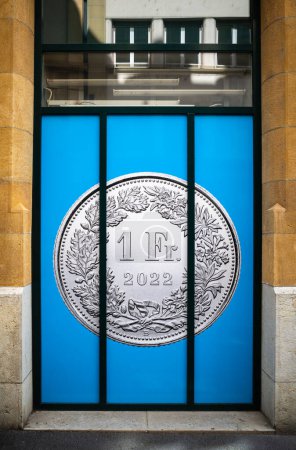 Photo for Neuchatel, Switzerland - August 7, 2023: Big swiss one franc coin in the picture behind bars of the bank window - Royalty Free Image