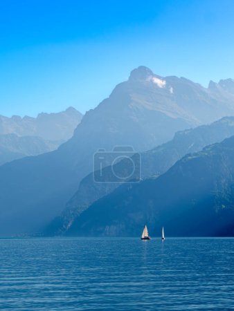 Téléchargez les photos : Contours des montagnes par le lac suisse Urnersee dans la lumière brumeuse de jour. Voiliers sur le lac - en image libre de droit