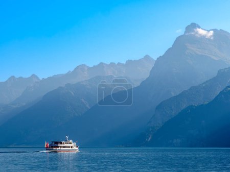 Téléchargez les photos : Contours des montagnes par le lac suisse Urnersee dans la lumière brumeuse de jour. Navire touristique sur le lac. - en image libre de droit