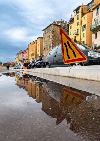 Téléchargez les photos : Les panneaux routiers, les voitures et les maisons à Menton se reflètent dans une flaque d'eau après la pluie - en image libre de droit