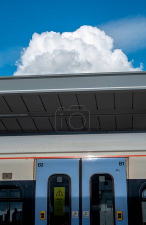 A large cloud in a blue sky over a train station in London, directly above the train door