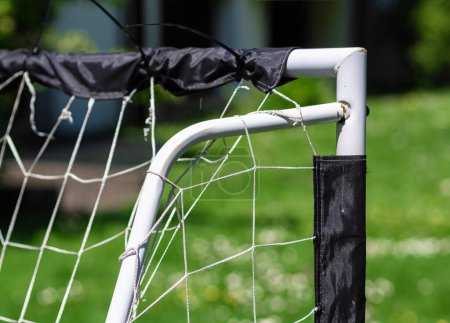 Close-up of a DIY soccer goal made of white PVC pipes with a worn net in a park setting, perfect for recreational or community sports themes.