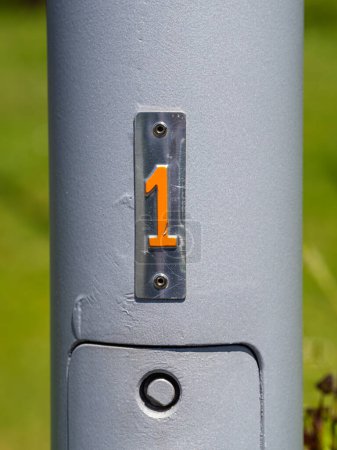 Close-up shot of a metallic pole with the number 1 in bright orange against a grey background.