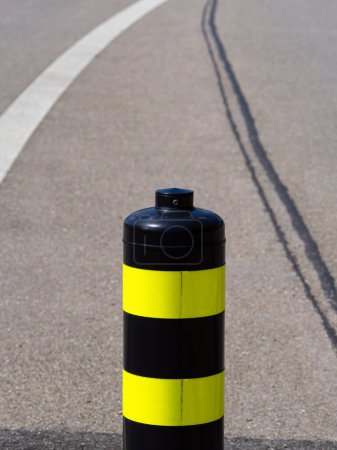 A close-up of a black bollard with yellow stripes on an asphalt road and white marking line