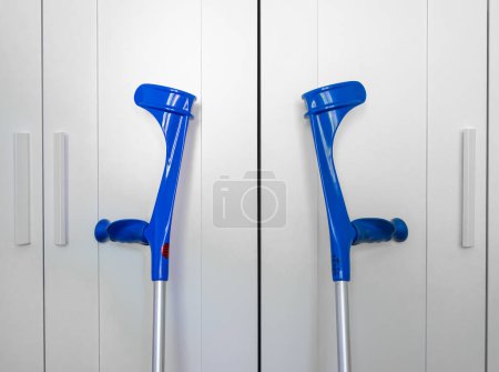 Two blue crutches symmetrically positioned against a white cupboard.