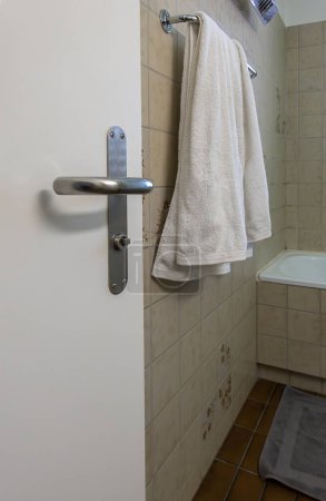 Ajuste de baño con toalla en la manija de la puerta, azulejos florales y bañera. Neutralmente coloreado, espacio funcional.
