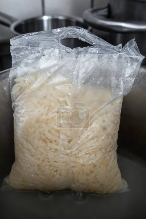 Una escena de cocina con una cacerola de metal en una estufa eléctrica, arroz precocinado en una bolsa de plástico cocinando en un agua.