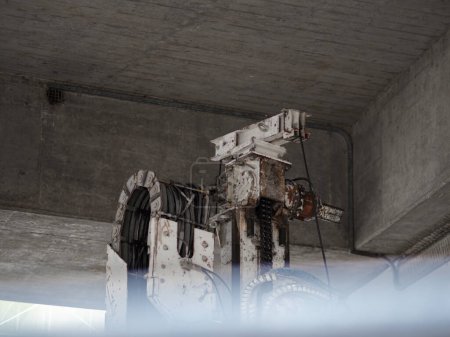 Una máquina industrial blanca oxidada bajo una estructura de hormigón. Utilizado probablemente en proyectos de infraestructura a gran escala.