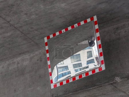Ein konvexer Verkehrsspiegel mit rot-weißem Rahmen spiegelt ein modernes Gebäude mit großen Fenstern wider. Es hilft bei der Navigation im toten Winkel.