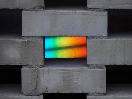 Eine Nahaufnahme aus grauen Betonsteinen mit einem Regenbogenlichtspalt, die vor neutralem Hintergrund lebendige Farben erzeugt.