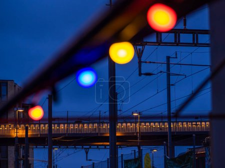 Zurich, Switzerland - May 16, 2024: A vibrant night scene with colorful lights in the foreground, a modern bridge and power lines in the background, and a twilight sky.