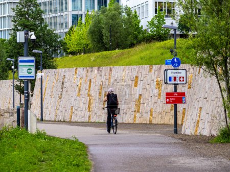 Photo for Basel, Switzerland - May 18, 2024: A person cycles on a lush pathway towards a signpost showing direction to border between France and Switzerland - Royalty Free Image