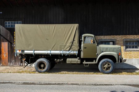 Olten, Suisse - 25 mai 2024 : Camion militaire vintage stationné près d'un bâtiment à matériaux mixtes en zone rurale.