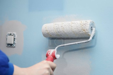 Gros plan d'une femme peignant le mur de sa maison avec un rouleau d'une couleur plus claire que l'ancien